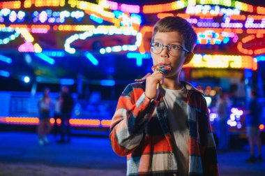 Beyaz bir çocuk, bir çocuk, eğlence parkına eğlenmek, oynamak ve atlıkarıncaya binmek için geldi. Atlıkarıncanın önünde duran bir çocuk.