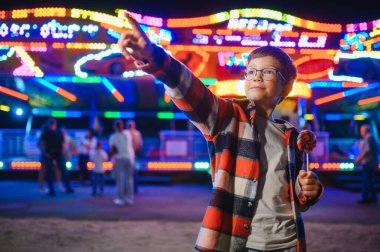 Akşamları eğlence parkında ya da sirkte renkli bir lolipop yiyen beyaz bir çocuk..