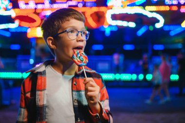 Akşamları eğlence parkında ya da sirkte renkli bir lolipop yiyen beyaz bir çocuk..