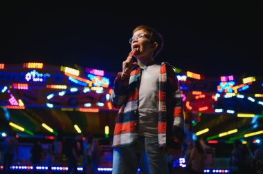 Akşamları eğlence parkında ya da sirkte renkli bir lolipop yiyen beyaz bir çocuk..