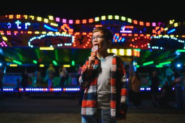 Beyaz bir çocuk, bir çocuk, eğlence parkına eğlenmek, oynamak ve atlıkarıncaya binmek için geldi. Atlıkarıncanın önünde duran bir çocuk.