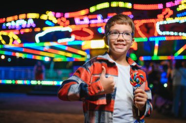 Akşamları eğlence parkında ya da sirkte renkli bir lolipop yiyen beyaz bir çocuk..