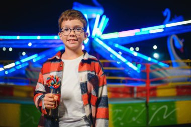 Beyaz bir çocuk, bir çocuk, eğlence parkına eğlenmek, oynamak ve atlıkarıncaya binmek için geldi. Atlıkarıncanın önünde duran bir çocuk.