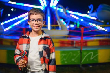 Akşamları eğlence parkında ya da sirkte renkli bir lolipop yiyen beyaz bir çocuk..