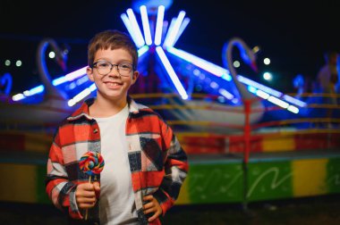 Akşamları eğlence parkında ya da sirkte renkli bir lolipop yiyen beyaz bir çocuk..