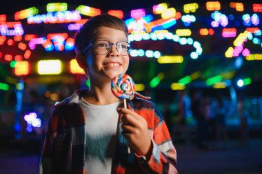 Akşamları eğlence parkında ya da sirkte renkli bir lolipop yiyen beyaz bir çocuk..
