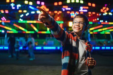 Akşamları eğlence parkında ya da sirkte renkli bir lolipop yiyen beyaz bir çocuk..
