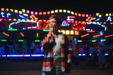 Akşamları eğlence parkında ya da sirkte renkli bir lolipop yiyen beyaz bir çocuk..