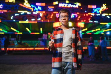 Akşamları eğlence parkında ya da sirkte renkli bir lolipop yiyen beyaz bir çocuk..