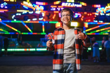 Akşamları eğlence parkında ya da sirkte renkli bir lolipop yiyen beyaz bir çocuk..