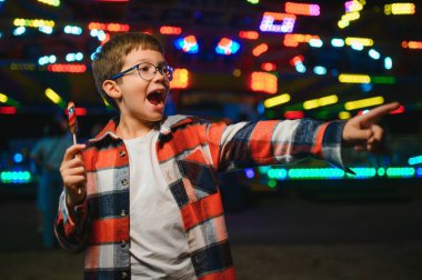 Akşamları eğlence parkında ya da sirkte renkli bir lolipop yiyen beyaz bir çocuk..