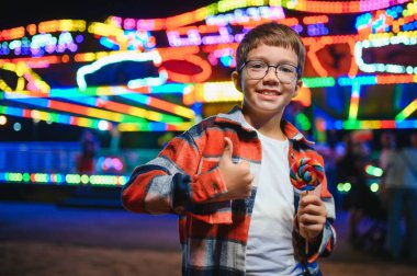 Akşamları eğlence parkında ya da sirkte renkli bir lolipop yiyen beyaz bir çocuk..