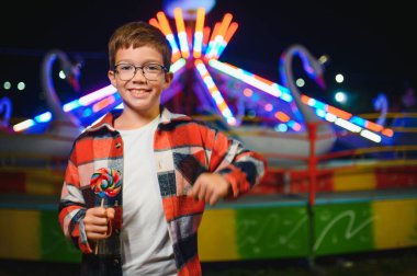 Beyaz bir çocuk, bir çocuk, eğlence parkına eğlenmek, oynamak ve atlıkarıncaya binmek için geldi. Atlıkarıncanın önünde duran bir çocuk.