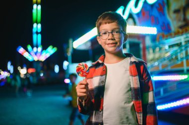 Beyaz bir çocuk, bir çocuk, eğlence parkına eğlenmek, oynamak ve atlıkarıncaya binmek için geldi. Atlıkarıncanın önünde duran bir çocuk.