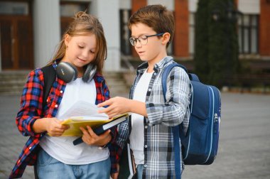 Bir grup ilkokul çocuğu kitap okuyorlar. Modern okul binası arka planında açık hava sınıfları var..