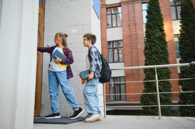 Çocuklar okula giriyor, büyük ahşap kapıyı açıyorlar. Güneşli bir günde okul kapısında sırt çantalı çocuklar. Akademik yılın başlangıcında. Seçici odaklı resim