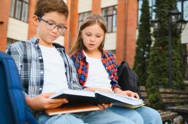 Çocuklar okul bahçesinde bankta oturarak kitap okurlar. Okula dönelim. Okul derslerinin başlangıcı..