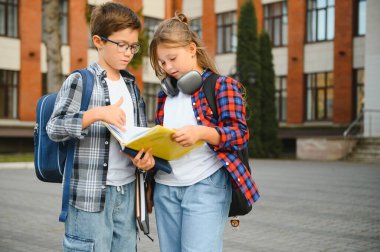 Bir grup ilkokul çocuğu kitap okuyorlar. Modern okul binası arka planında açık hava sınıfları var..