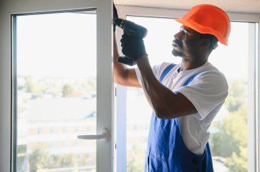 Tamirci, beyaz plastik pencereyi içeri ayarlıyor. İşçi, pencereyi onarmak için tornavida kullanıyor. ev ödevi.