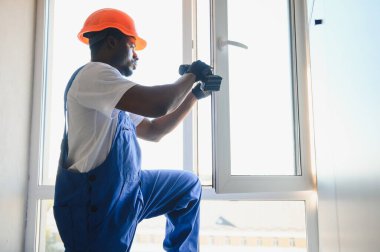 Tamirci, beyaz plastik pencereyi içeri ayarlıyor. İşçi, pencereyi onarmak için tornavida kullanıyor. ev ödevi.