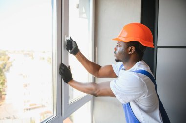 Evdeki oturma odasına plastik pencereler monte eden ya da ayarlayan işçi.