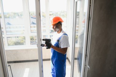 Evdeki oturma odasına plastik pencereler monte eden ya da ayarlayan işçi.