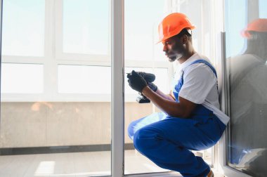 Tamirci, beyaz plastik pencereyi içeri ayarlıyor. İşçi, pencereyi onarmak için tornavida kullanıyor. ev ödevi.