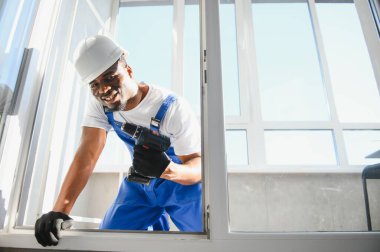 Tamirci, beyaz plastik pencereyi içeri ayarlıyor. İşçi, pencereyi onarmak için tornavida kullanıyor. ev ödevi.