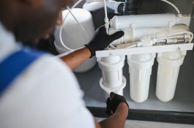 Technician installing reverse osmosis equipment under the sink. Front view. Horizontal composition.