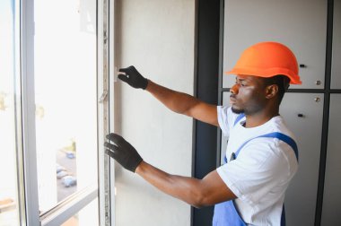 Evdeki oturma odasına plastik pencereler monte eden ya da ayarlayan işçi.