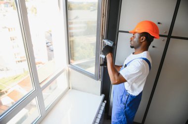 Tamirci, beyaz plastik pencereyi içeri ayarlıyor. İşçi, pencereyi onarmak için tornavida kullanıyor. ev ödevi.