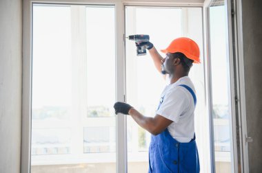 Evdeki oturma odasına plastik pencereler monte eden ya da ayarlayan işçi.