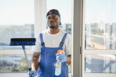 Önlüklü Afrikalı profesyonel temizlik işçisi pencereleri özel ekipmanlarla temizliyor..