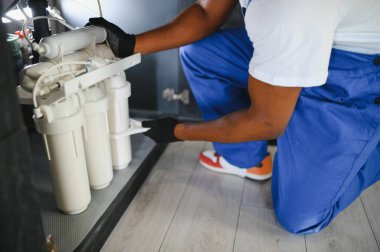 Tesisatçı su filtresi kurar ya da değiştirir. Yerleştirme su filtresi. Tamirci mutfağa su filtresi koyuyor. Ters osmoz su arıtma sisteminin kurulumu.