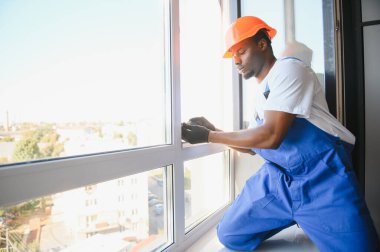 Evdeki oturma odasına plastik pencereler monte eden ya da ayarlayan işçi.