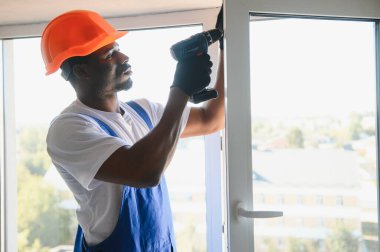Tamirci, beyaz plastik pencereyi içeri ayarlıyor. İşçi, pencereyi onarmak için tornavida kullanıyor. ev ödevi.