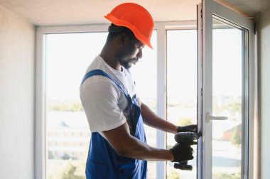 Tamirci, beyaz plastik pencereyi içeri ayarlıyor. İşçi, pencereyi onarmak için tornavida kullanıyor. ev ödevi.