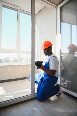 Evdeki oturma odasına plastik pencereler monte eden ya da ayarlayan işçi.