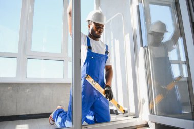 Evdeki oturma odasına plastik pencereler monte eden ya da ayarlayan işçi.