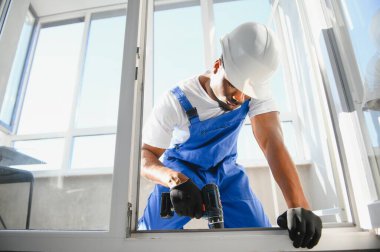 Evdeki oturma odasına plastik pencereler monte eden ya da ayarlayan işçi.