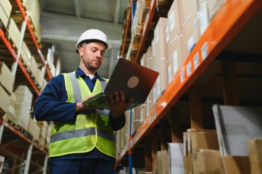 Depodaki adam teslimatı kontrol ediyor, depodaki stoklar dizüstü bilgisayarda. Depo yöneticisi depo yönetimi yazılımı, uygulama kullanıyor.