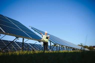 Güneş çiftliği, mühendis ile güneş paneli sistemin işleyişini kontrol eder, dünyanın enerjisini korumak için alternatif enerji, temiz enerji üretimi için fotovoltaik modül fikri.