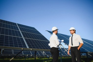Güneş paneli çiftliği. İki Avrupalı mühendis güneş panellerini inceliyor. Güneş paneli çiftliğindeki işçiler.