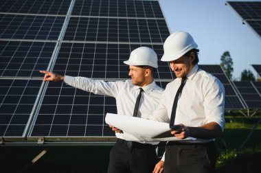 Güneş paneli çiftliği. İki Avrupalı mühendis güneş panellerini inceliyor. Güneş paneli çiftliğindeki işçiler.