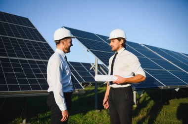Güneş paneli çiftliği. İki Avrupalı mühendis güneş panellerini inceliyor. Güneş paneli çiftliğindeki işçiler.