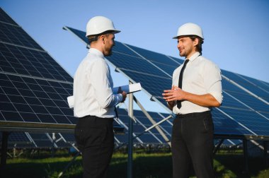 Güneş çiftliği, güneş paneli ve iki mühendis sistemin işleyişini kontrol etmek için yürür, dünyanın enerjisini korumak için alternatif enerji, temiz enerji üretimi için fotovoltaik modül fikri.