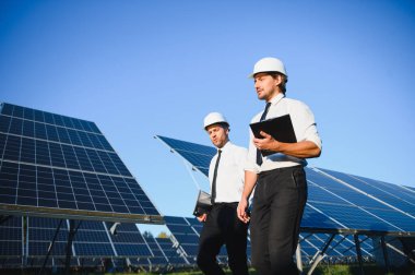 Güneş çiftliği, güneş paneli ve iki mühendis sistemin işleyişini kontrol etmek için yürür, dünyanın enerjisini korumak için alternatif enerji, temiz enerji üretimi için fotovoltaik modül fikri.