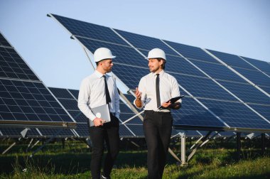 Güneş paneli çiftliği. İki Avrupalı mühendis güneş panellerini inceliyor. Güneş paneli çiftliğindeki işçiler.
