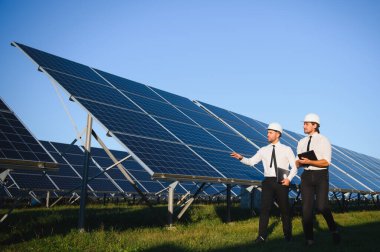 Yenilenebilir enerji. Bir güneş paneli çiftliğinin arka planında iki mühendis..