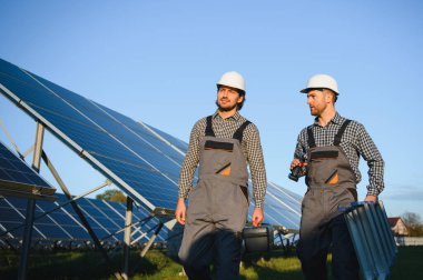 Gri üniforma giyen iki yetenekli işçi veya zanaatkar, teknisyenler temiz enerji ve elektrik tedariği için güneş panelleri kuruyorlar..
